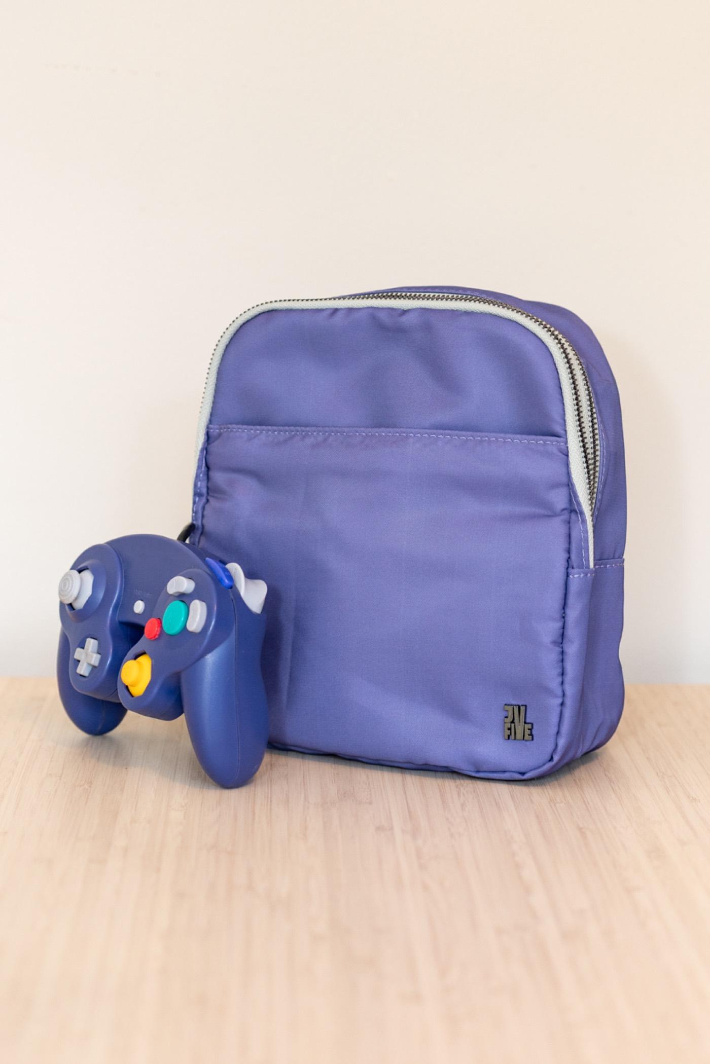 The BagCube Console Bag in GameCube purple beside an indigo GameCube controller